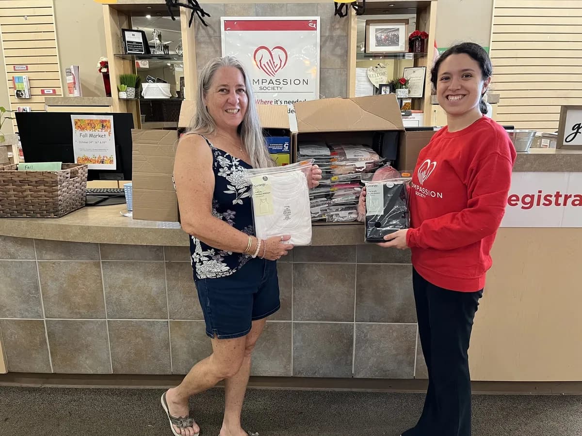 A Compassion Society of Halton volunteer in a red Compassion sweatshirt receives a donation of new clothing items at the front desk.