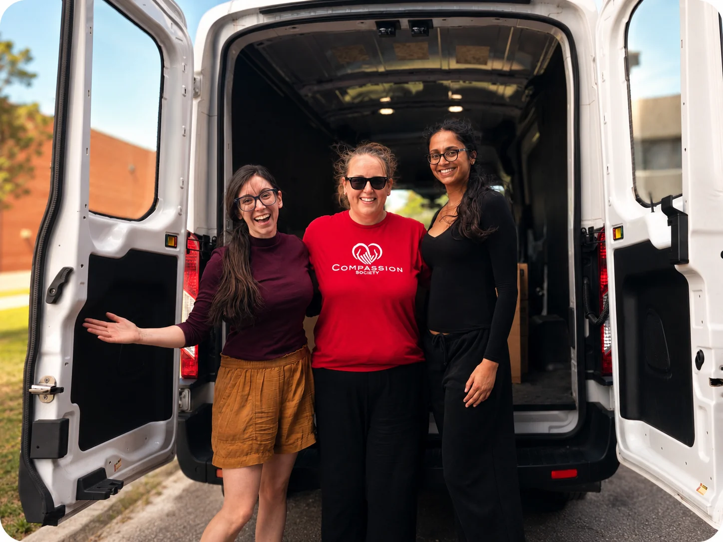 Three Compassion Society of Halton volunteers stand together, smiling, at the open back doors of a cargo van, one wearing a Compassion Society t-shirt.