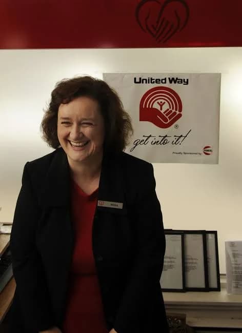 Mina Wahidi smiling, wearing a name tag, standing in front of a United Way Halton banner.
