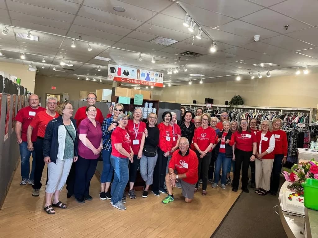 A large team of Compassion Society of Halton volunteers and staff gather together inside the clothing program space.