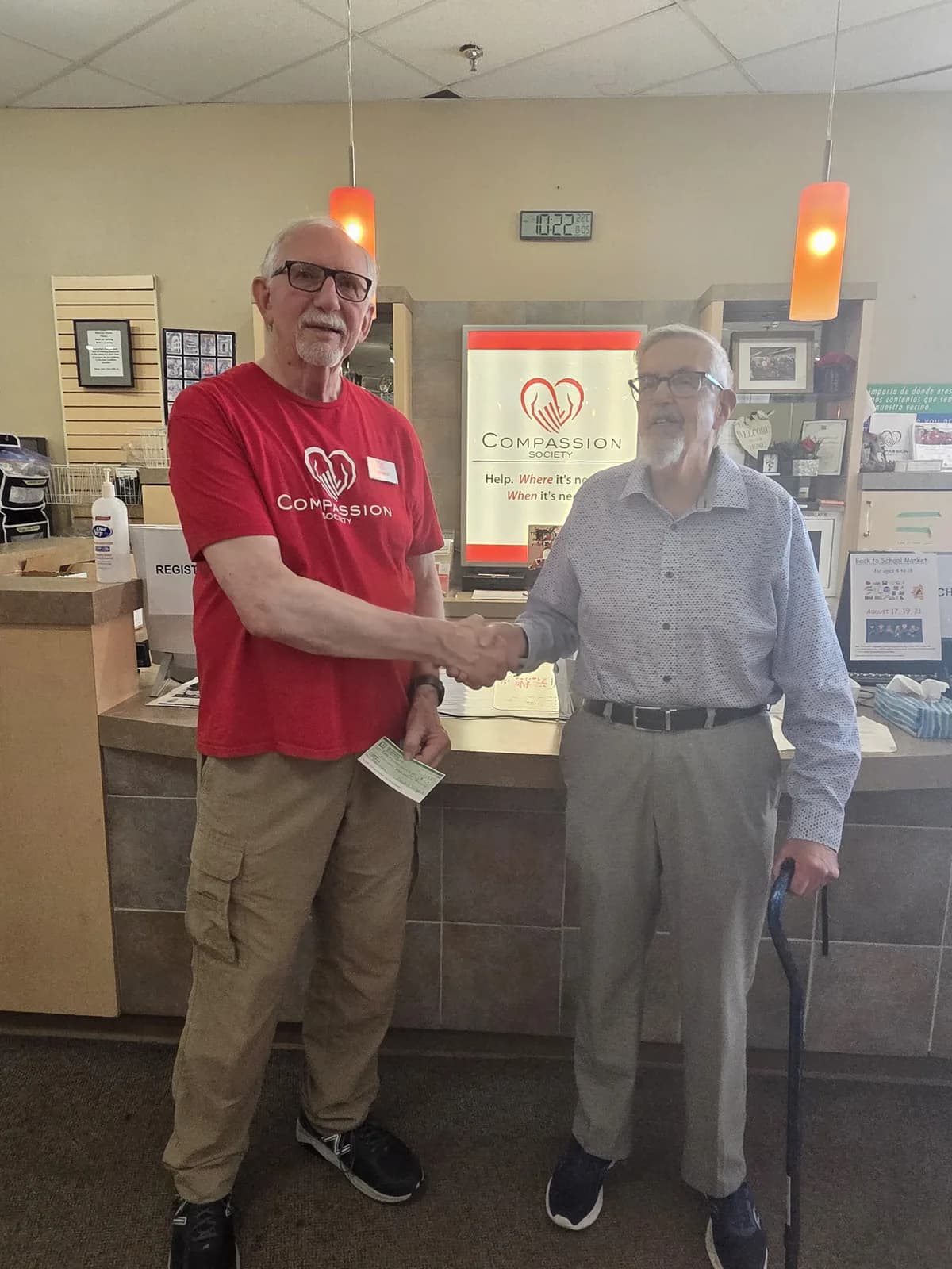 Two Compassion Society of Halton team members sharing a warm handshake at the reception desk, one in a red Compassion Society t-shirt.