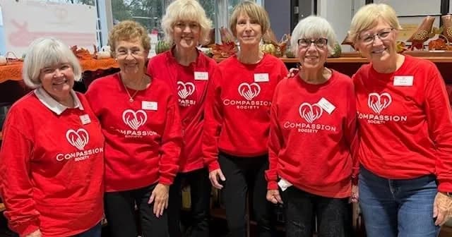 Six Compassion Society of Halton volunteers in matching red Compassion sweatshirts, smiling together.