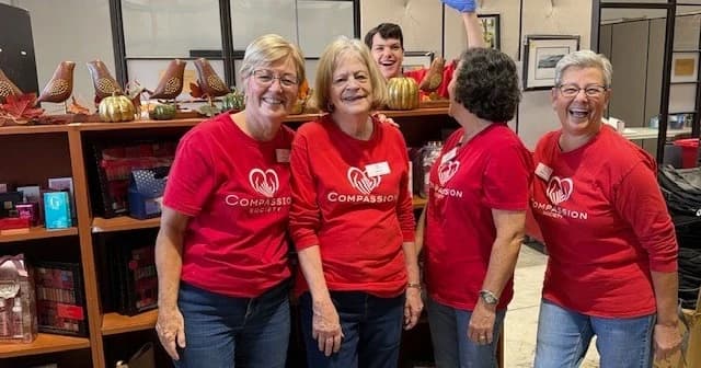 Four Compassion Society of Halton volunteers in red shirts, laughing together in the store.