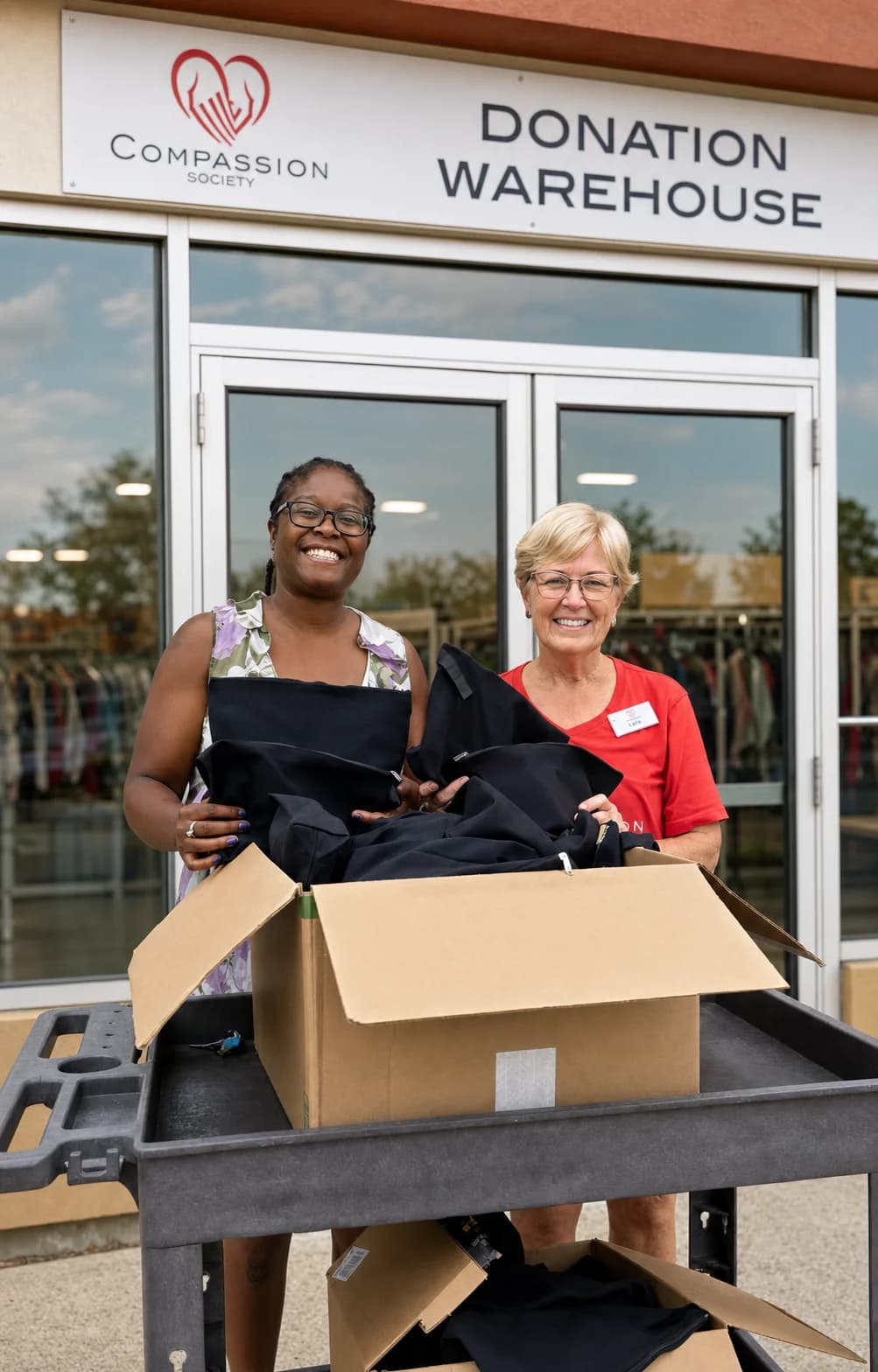Two women standing with donated clothing outside the Compassion Society of Halton Donation Warehouse.